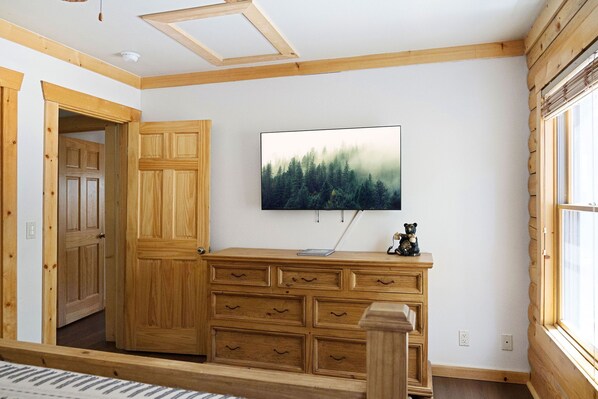 Une pièce avec une commode en bois, un téléviseur fixé au mur et une grande fenêtre.