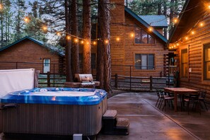A wooden cabin with a hot tub, barbecue, and outdoor seating area.
