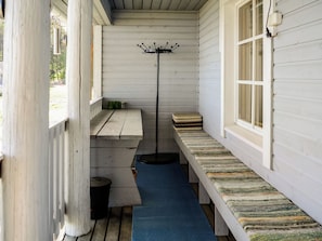 En smal veranda med en blå matta, en svart golvlampa och en bänk med en mönstrad kudde.