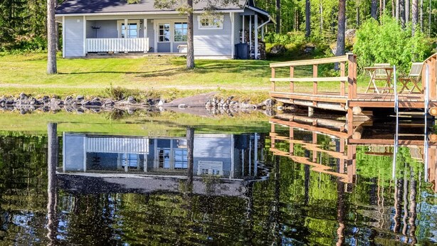 Een chalet met een steiger die uitsteekt in een rustig meer, omringd door bomen.