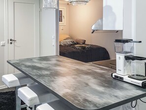 Ett litet kök med en arbetsbänk, en kaffebryggare och en dörr som leder in till ett sovrum.