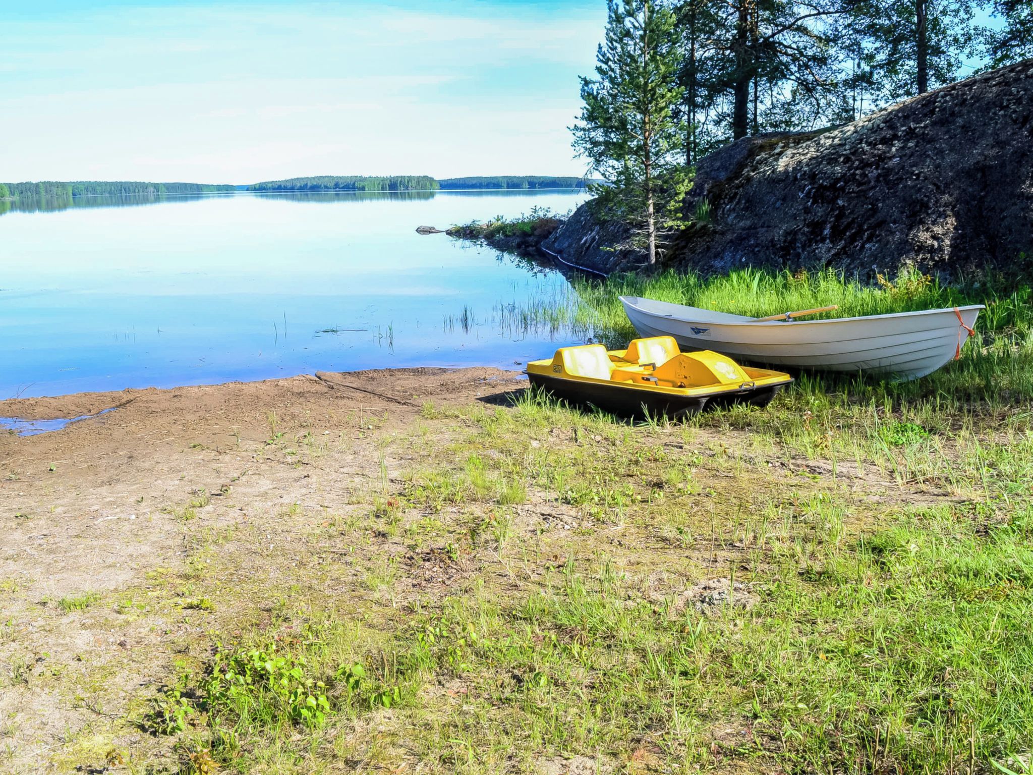 Un lac paisible aux rives verdoyantes, un petit bateau amarré au bord, et un autre bateau jaune posé sur l’herbe.