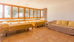 A room with two beds, a sofa, and large windows.