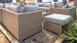 A wicker outdoor seating area with cushions, a small table, and a bench.