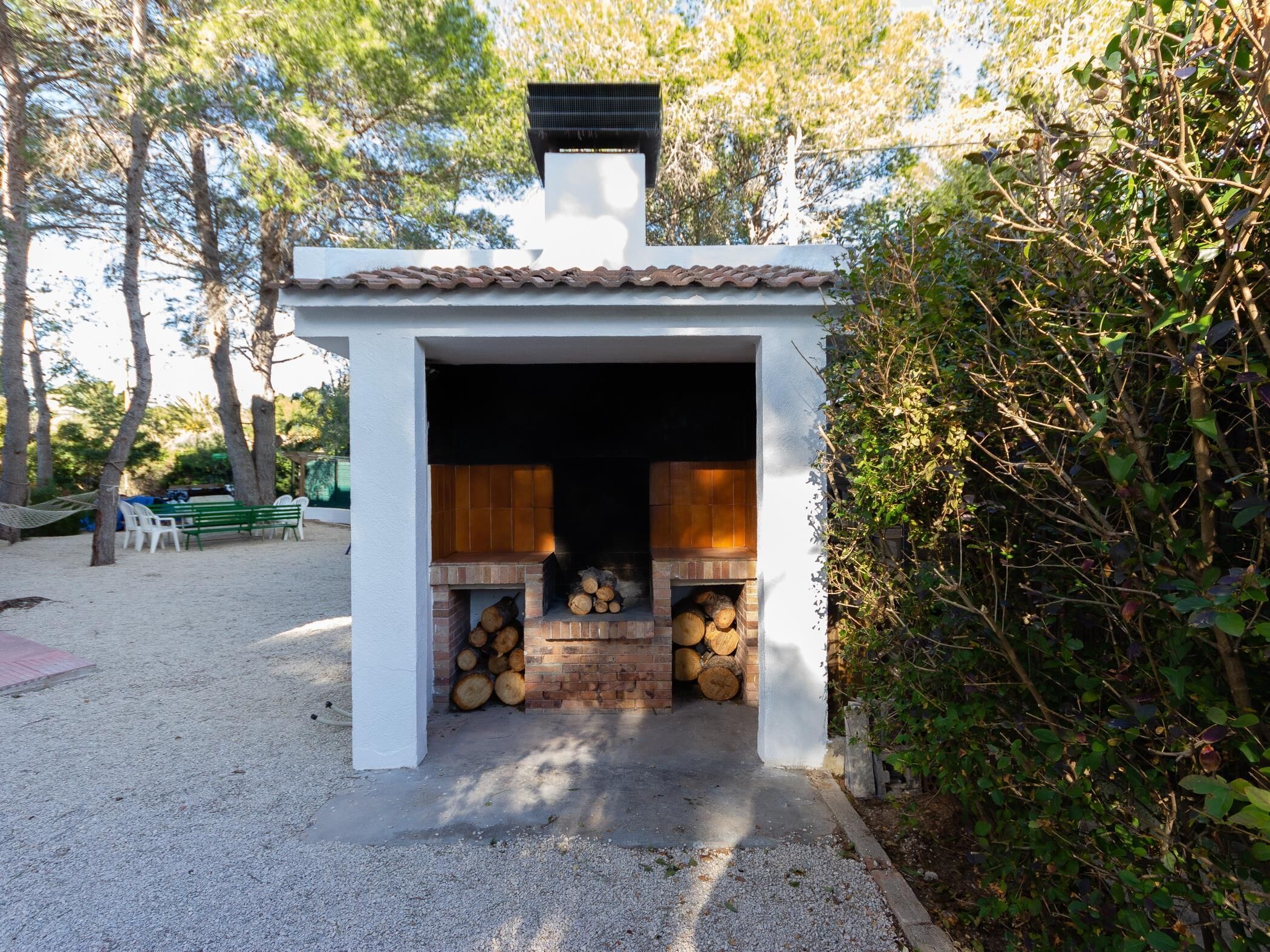 Une petite cheminée d’extérieur avec un toit en tuiles, entourée d’arbres et agrémentée d’un banc.