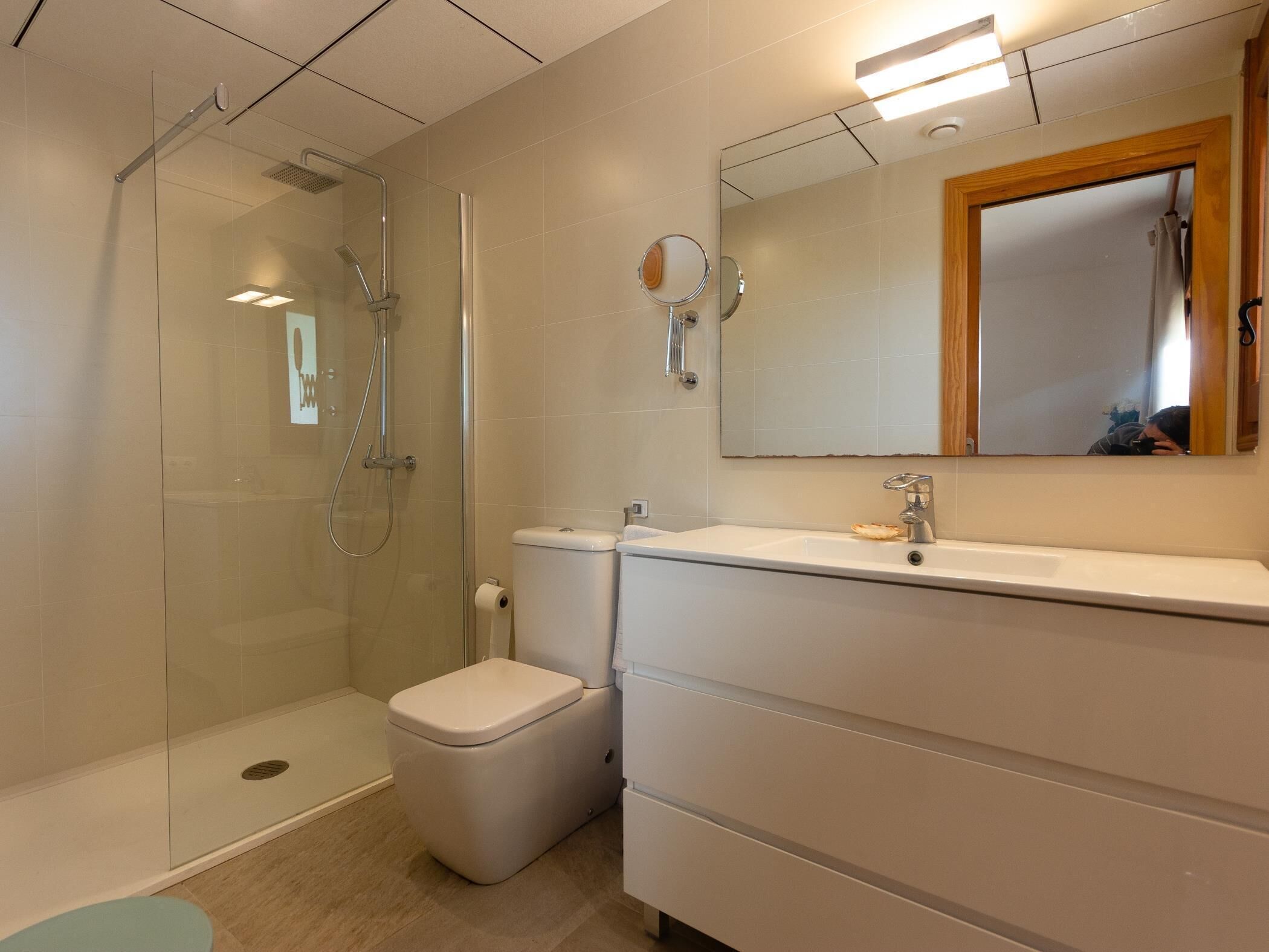 Une salle de bain moderne avec une douche à parois de verre, des toilettes blanches et un meuble-lavabo avec un miroir.