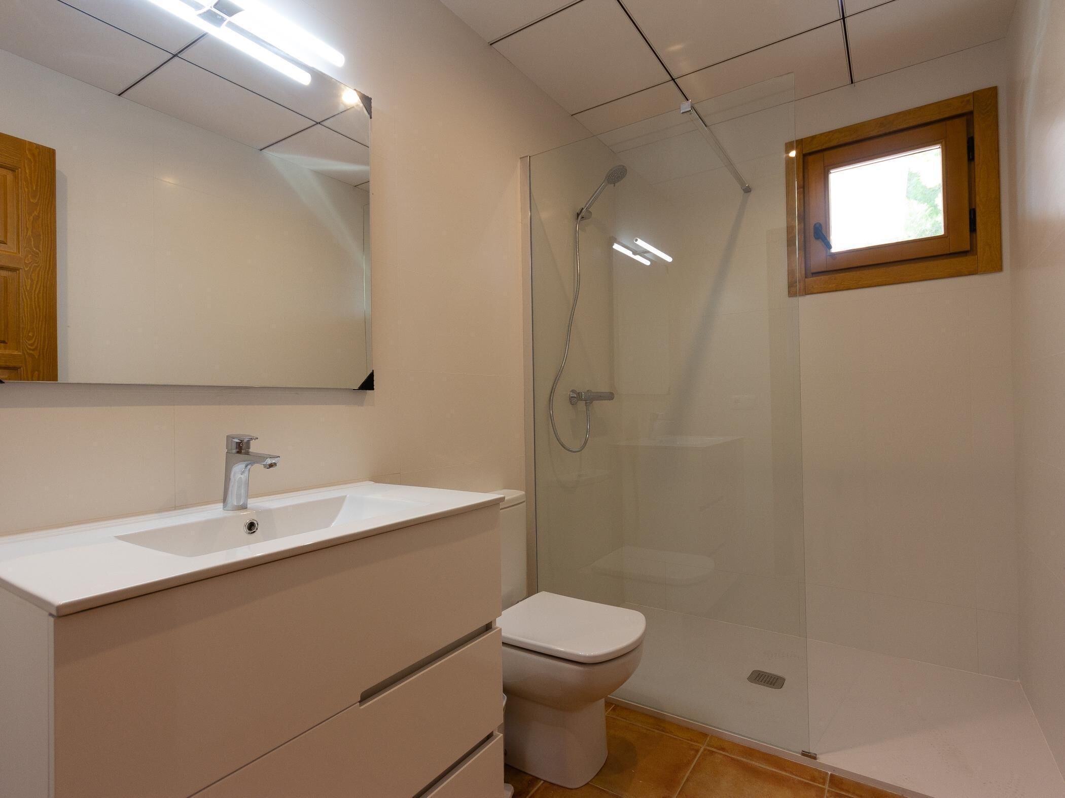 Un baño con lavamanos blanco, inodoro y ducha con mampara de vidrio.