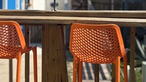 A wooden table with two orange chairs, a metal umbrella, and a view of the sea and buildings in the background. - Ocean View, Short Walk to Beach, Free Golf Cart Included (Port Aransas)