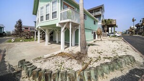 A two-story house with a balcony, a palm tree in front, and a sandy area with wooden posts. - Ocean View, Short Walk to Beach, Free Golf Cart Included (Port Aransas)