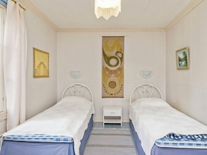 Een kamer met twee eenpersoonsbedden, een klein nachtkastje, een wandlamp en een ingelijst kunstwerk.