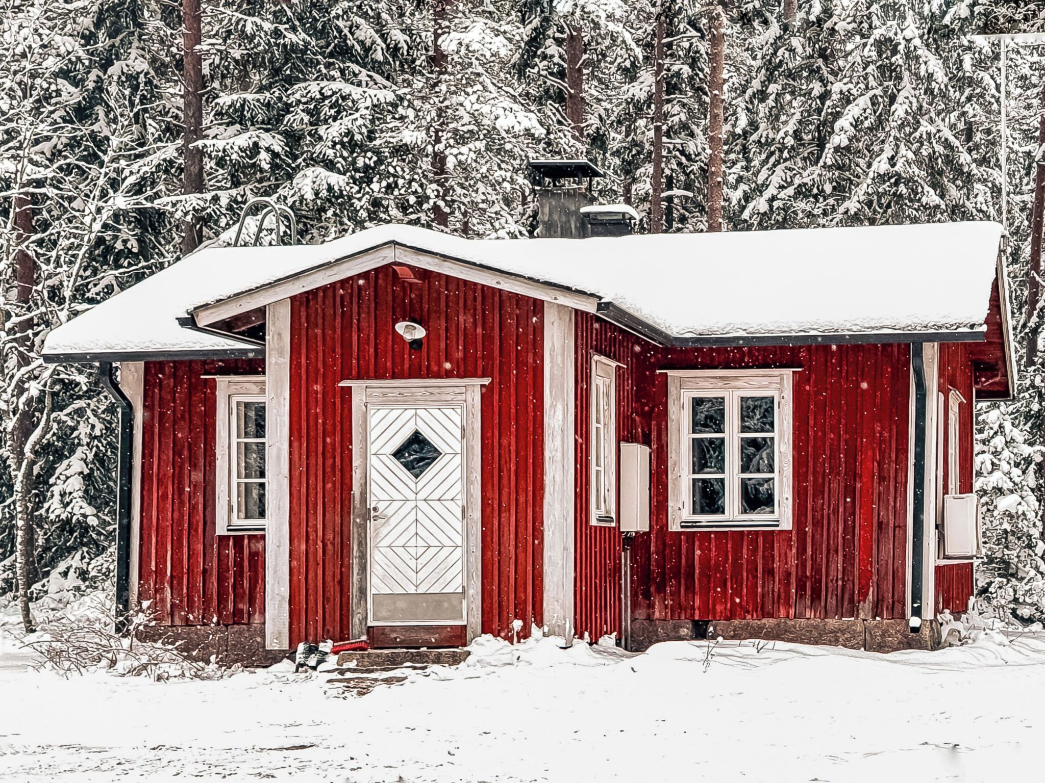 Eine rote Holzhütte mit weißer Tür und Fenstern, umgeben von schneebedeckten Bäumen.