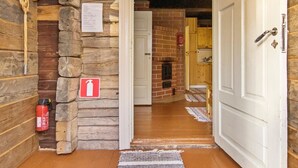 Een houten blokhut van binnen, met een stenen muur, een witte deur en een brandblusser.