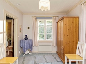 Een kamer met een groot raam, een houten garderobe, een klein tafeltje met een vaas en een stoel.