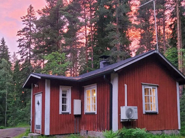 A small red cabin with a white door, windows, and an air conditioning unit.