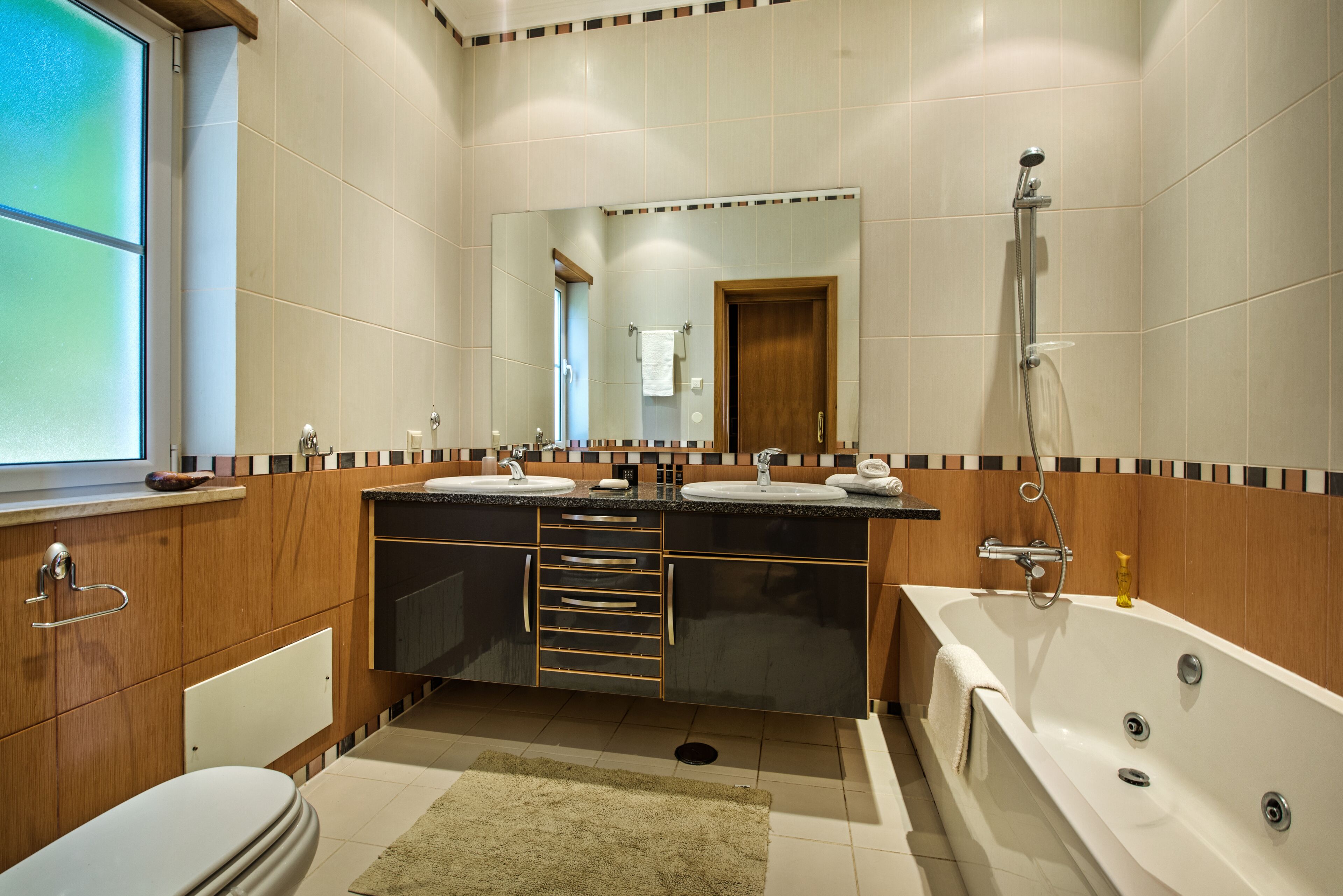 A modern bathroom with a large mirror, two sinks, a bathtub, and wooden cabinetry.
