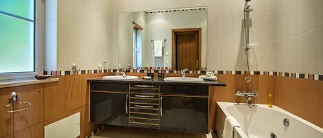 A modern bathroom with a large mirror, two sinks, a bathtub, and wooden cabinetry.