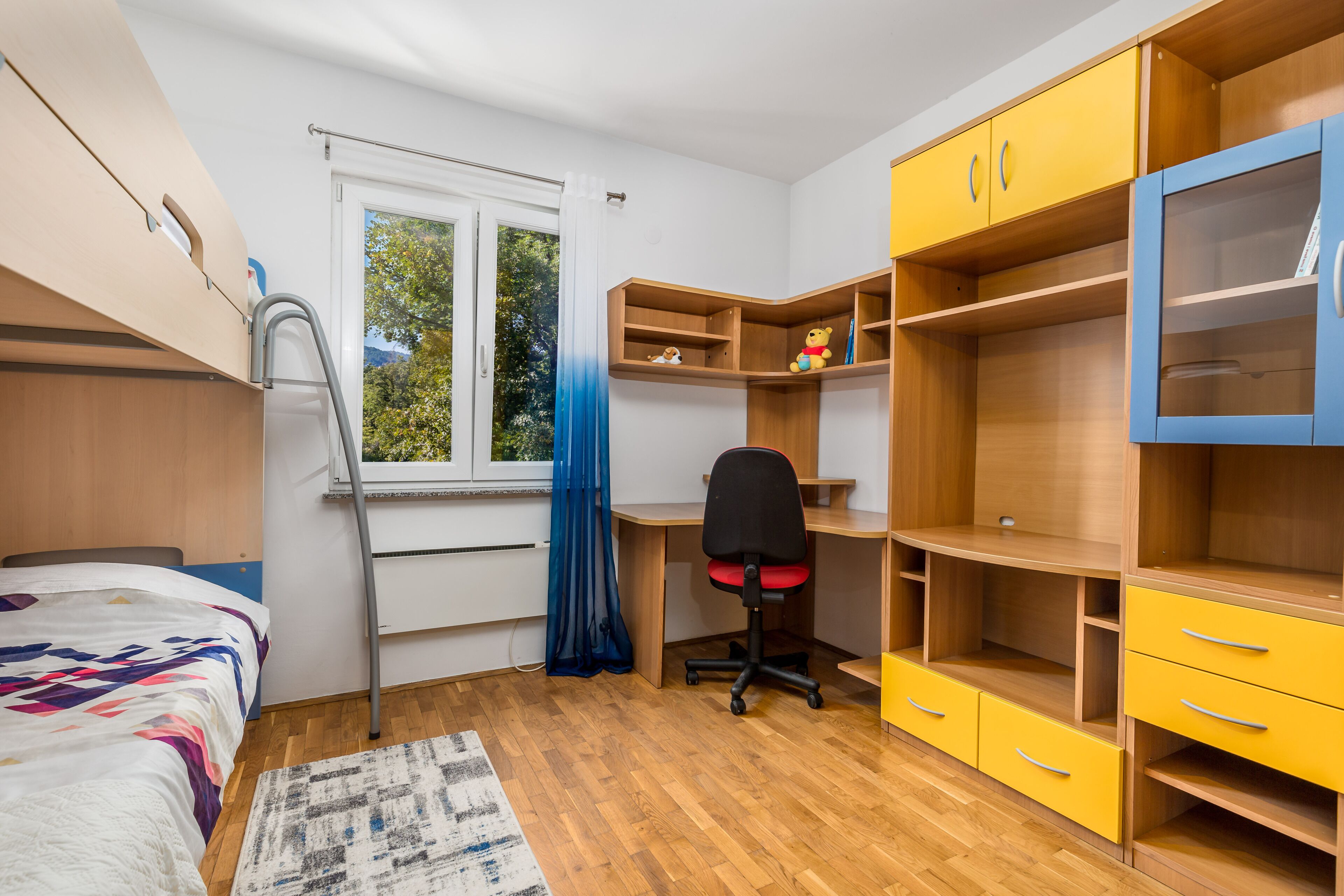 A bedroom with a bed, a desk, a chair, and built-in shelving.