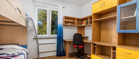 A bedroom with a bed, a desk, a chair, and built-in shelving.