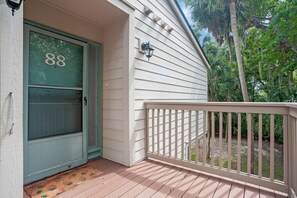 Une maison avec une porte verte portant le numéro « 88 », une façade blanche et une terrasse en bois dotée d’une balustrade.