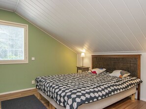 A bedroom with a sloped ceiling, a bed with patterned bedding, a bedside lamp, and a window with blinds. - Isokoskelo by Interhome (Pertunmaa)