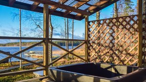 Een houten terras met een jacuzzi, houten spijlen en uitzicht op een meer en een steiger.