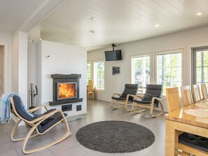 A living room with a fireplace, rocking chairs, a dining table, and large windows.