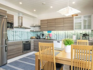 A modern kitchen with wooden cabinets, stainless steel appliances, and a dining area with a table and chairs. - Isokoskelo by Interhome (Pertunmaa)