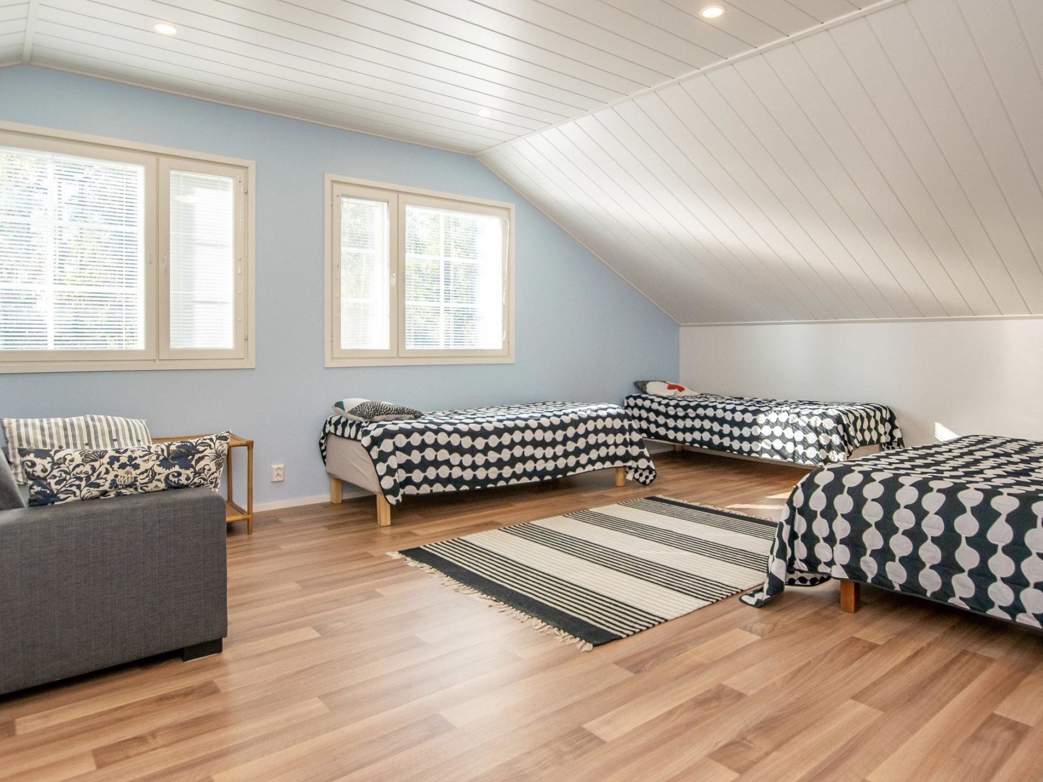 Habitación amplia con dos camas, un sofá y ventanas grandes.