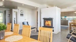 Een moderne woonkamer met een open haard, houten meubels en een keuken in de achtergrond.