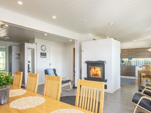 A modern living room with a fireplace, dining area with wooden chairs and a table, and a kitchen area with wooden cabinets. - Isokoskelo by Interhome (Pertunmaa)