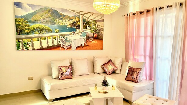 Ein Wohnzimmer mit einem weißen Sofa, zwei Hocker, einem Couchtisch und einem Gemälde einer Küstenlandschaft.