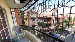Ein Balkon mit Metallgeländer, einem weißen Stuhl und Blick auf eine Straße mit parkenden Autos und Gebäuden.