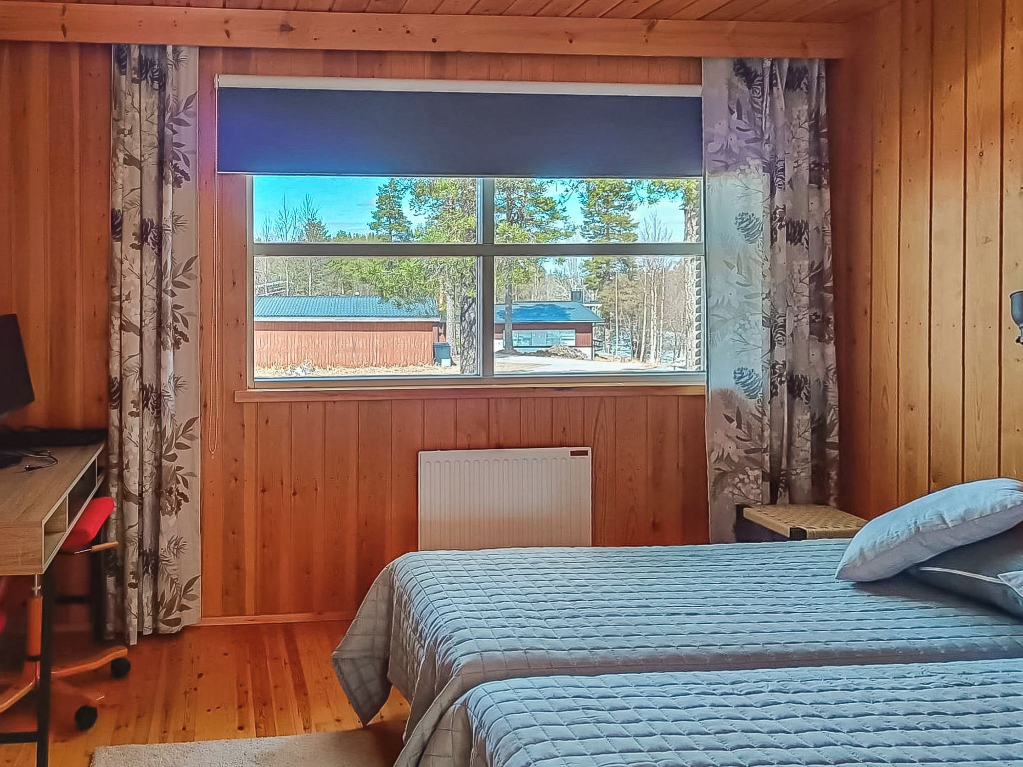 Une chambre avec un lit, un bureau et une fenêtre donnant sur un immeuble et des arbres.