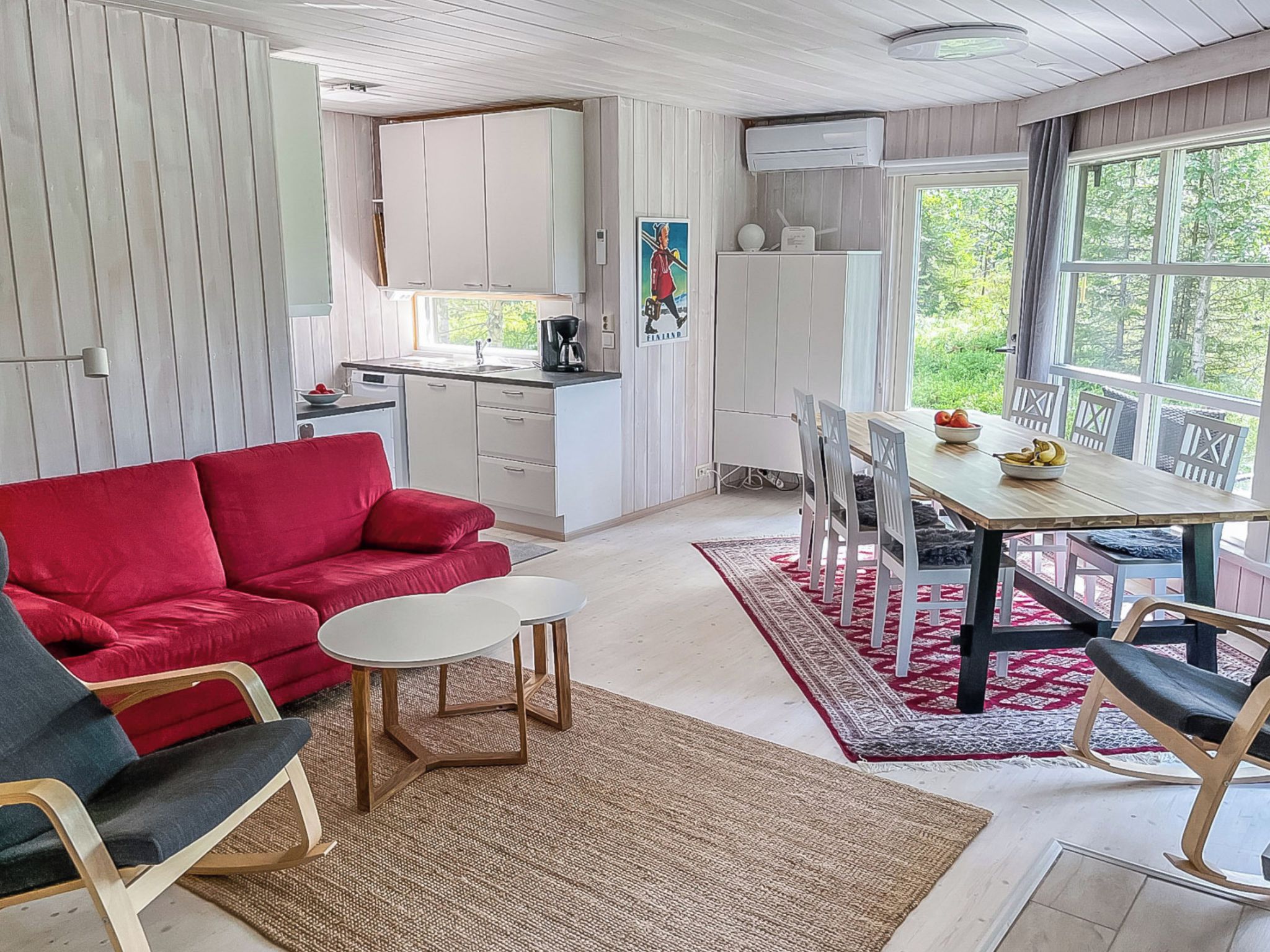 A compact living space with a red sofa, a small round table, a kitchen area with white cabinets, and a dining table with chairs.