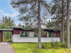 Una casa moderna con fachada blanca y detalles oscuros, rodeada de árboles y un césped.