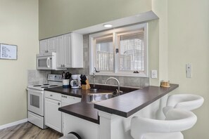 A compact kitchen with white cabinets, a microwave, a stove, and a sink.