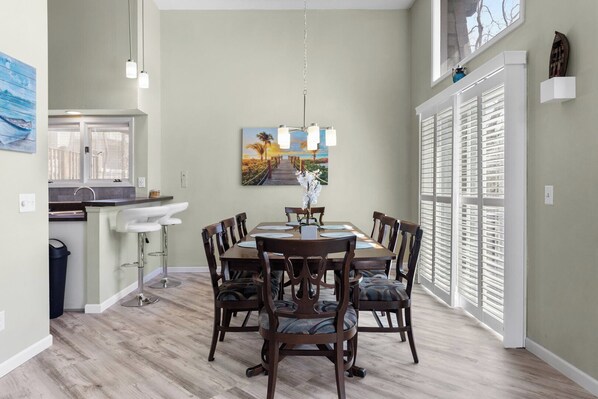 A dining area with a wooden table and chairs, a pendant light, and a painting on the wall.