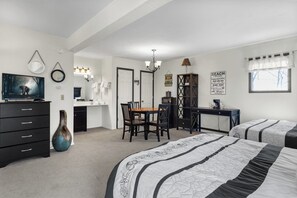 A bedroom with two beds, a desk, a chair, a dresser, a TV, and a mirror.