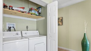 A laundry room with two washing machines, a shelf with various items, a door, and a green vase. - Anchors Away - Three Bedroom House, Sleeps 12 (Osage Beach)