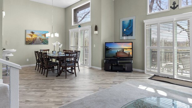 A dining area with a wooden table and chairs, a television on a stand, and a large window with blinds. - Anchors Away - Three Bedroom House, Sleeps 12 (Osage Beach)