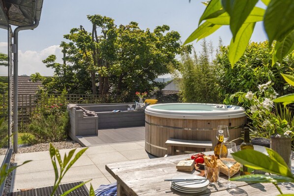 A hot tub in a garden with a wooden deck, surrounded by lush greenery and a wooden fence. - 6 The Dunes - Short walk to the beach - Hot Tub - Free Wi-Fi (Hayle)