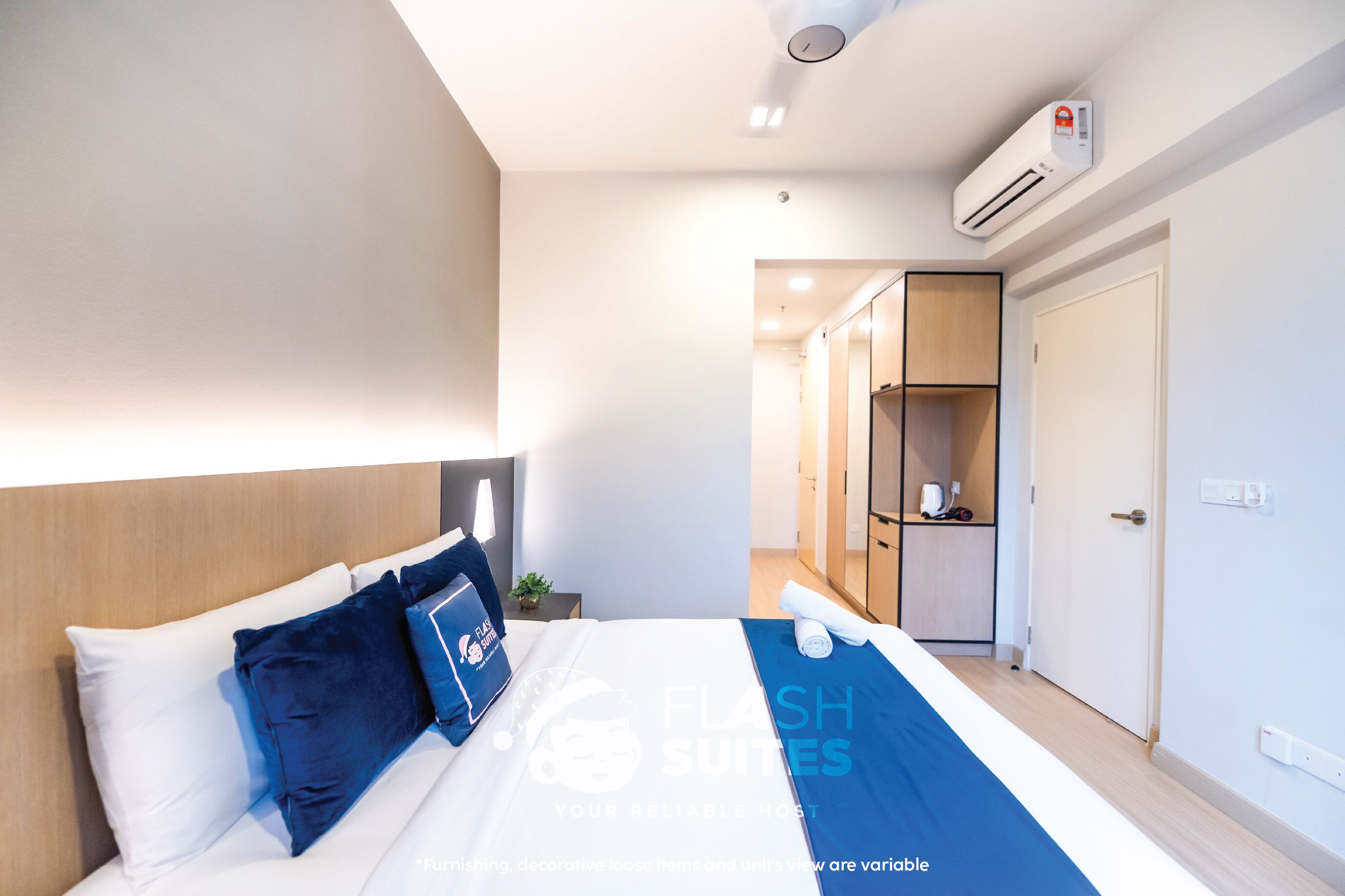 A modern hotel room with a neatly made bed, an air conditioning unit, a wardrobe, and a small table with a lamp.