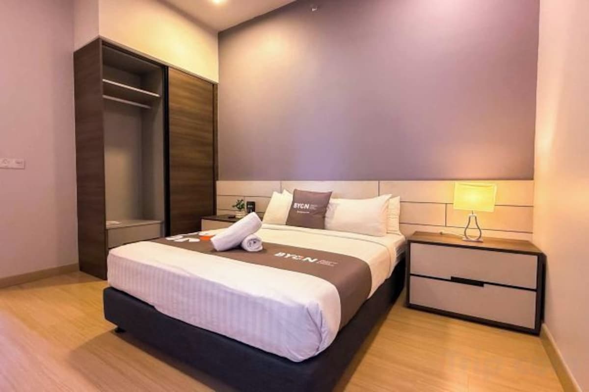 Een moderne hotelkamer met een groot bed, een kledingkast, een nachtkastje met een lamp en een bedtafel.