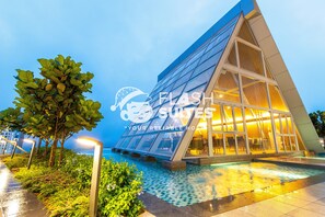 Un hôtel moderne doté d’une façade en verre, d’une piscine et d’une entrée bien éclairée.