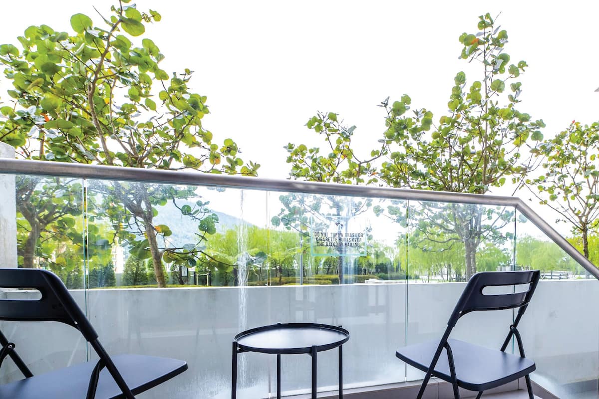 Un balcon avec deux chaises noires et une petite table ronde, donnant sur un jardin avec des arbres et un bâtiment en arrière-plan.