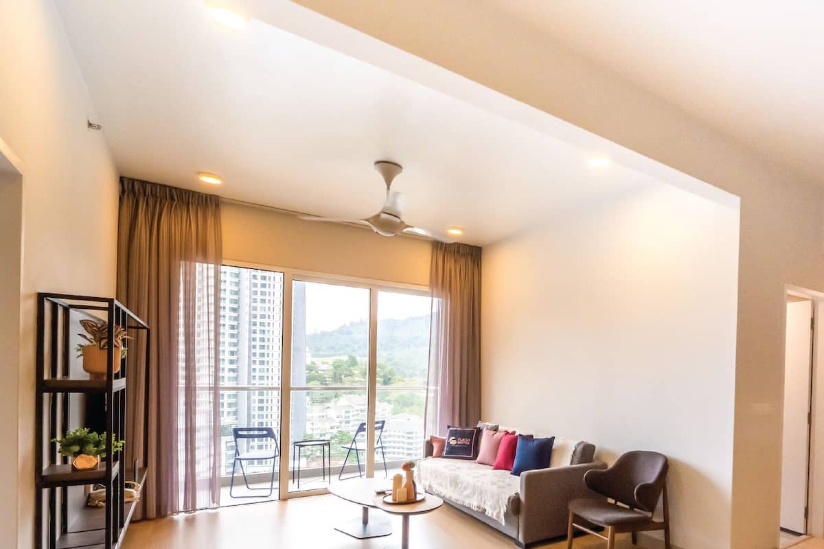 Un salon spacieux doté d’une grande fenêtre, d’un ventilateur de plafond, d’un canapé et d’un coin repas avec des chaises et une table.