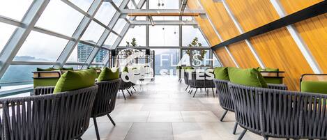 A modern interior with wicker chairs and green cushions, large windows, and a view of the city.