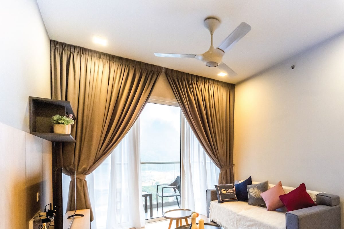 Une chambre d’hôtel moderne dotée d’une grande fenêtre, d’un ventilateur de plafond, d’un canapé avec des coussins et d’une petite table.