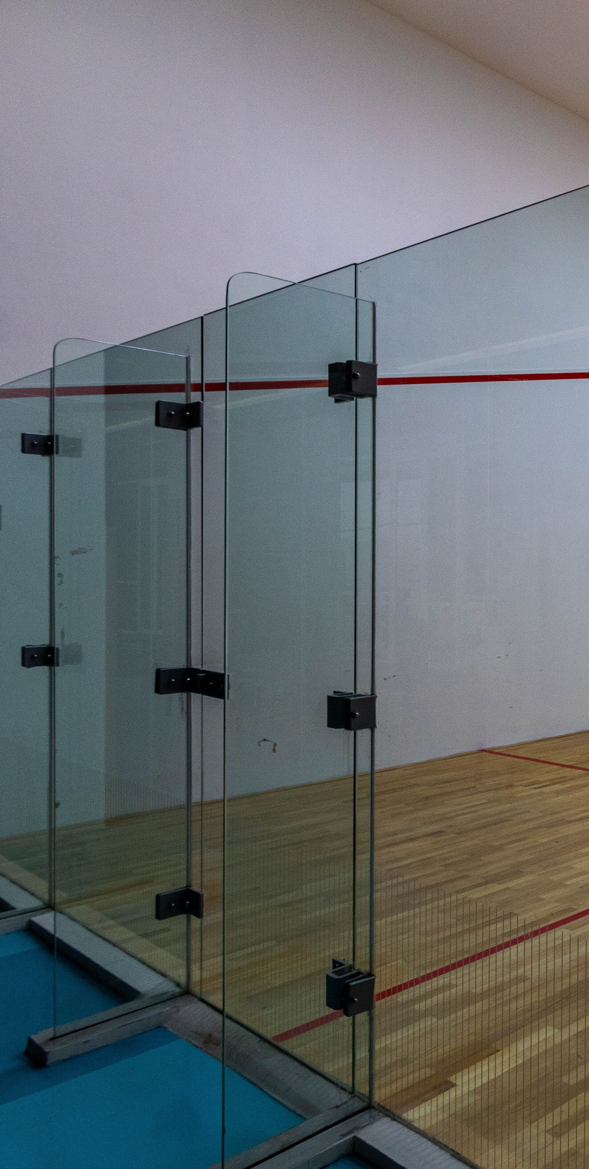Ein Squashplatz mit Glaswänden, Holzboden und einer roten Linie zur Markierung des Spielfelds.
