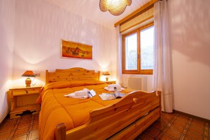A room with a wooden bed, a nightstand with a lamp, a window with curtains, and a painting on the wall. - Appartamento Secrel 10, Tremosine, Italy (Tremosine)